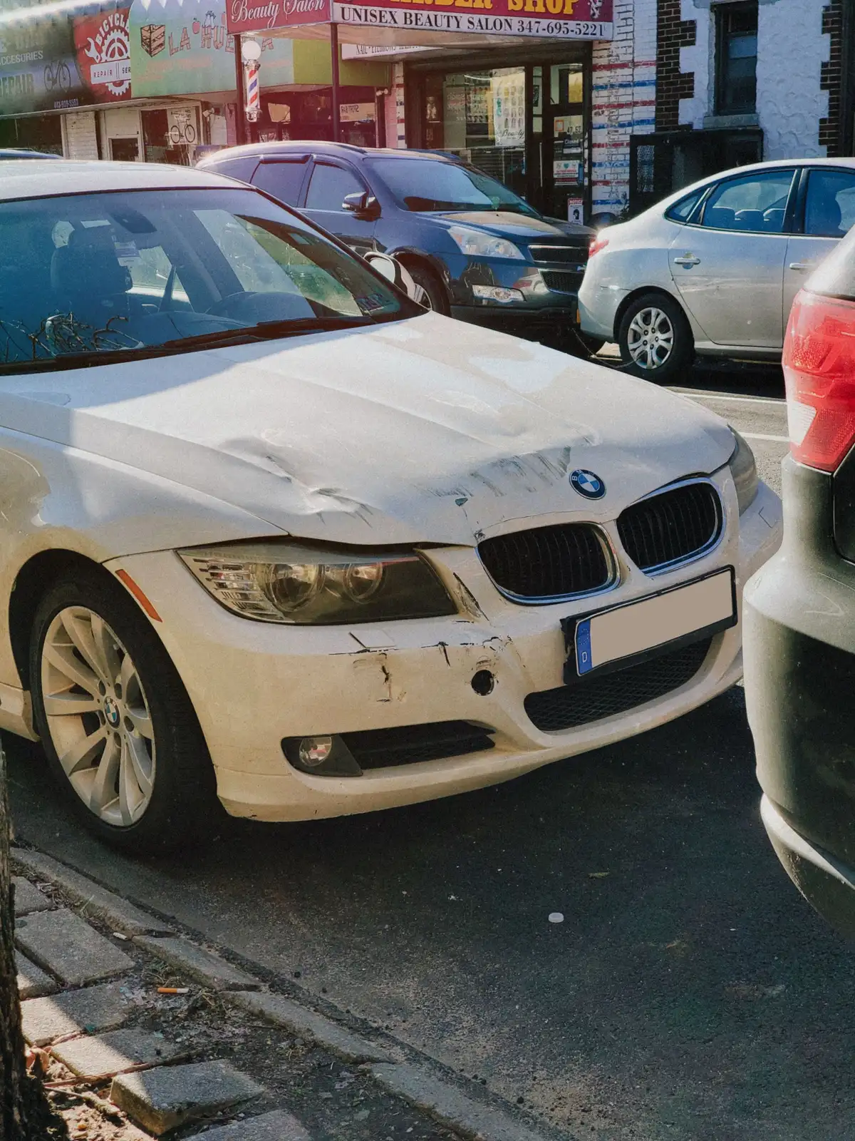 The crushed front of a white car in daylight, with trees behind it.